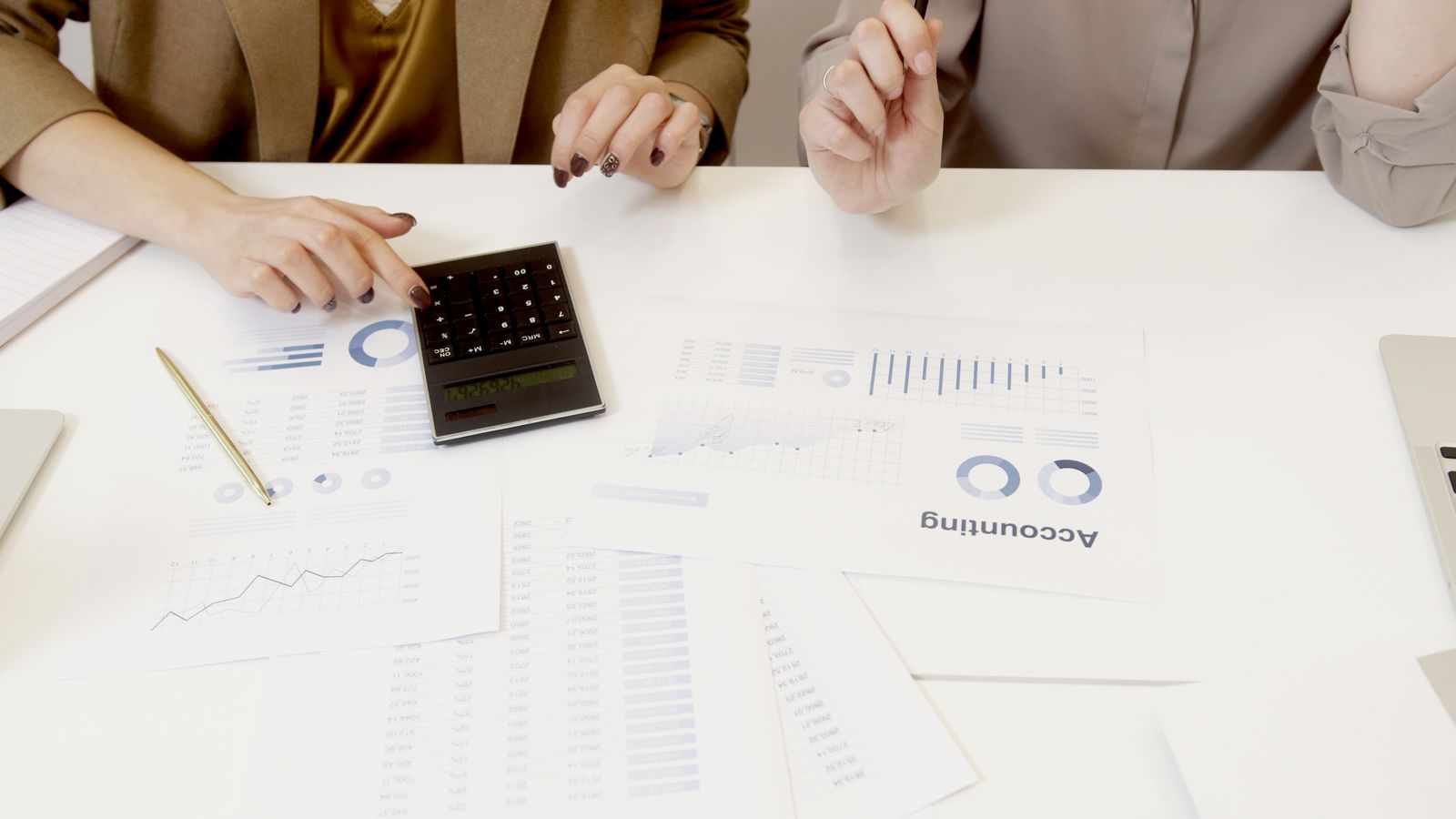 Two finance professionals reviewing an outsourced accounting proposal and scope of services with a calculator