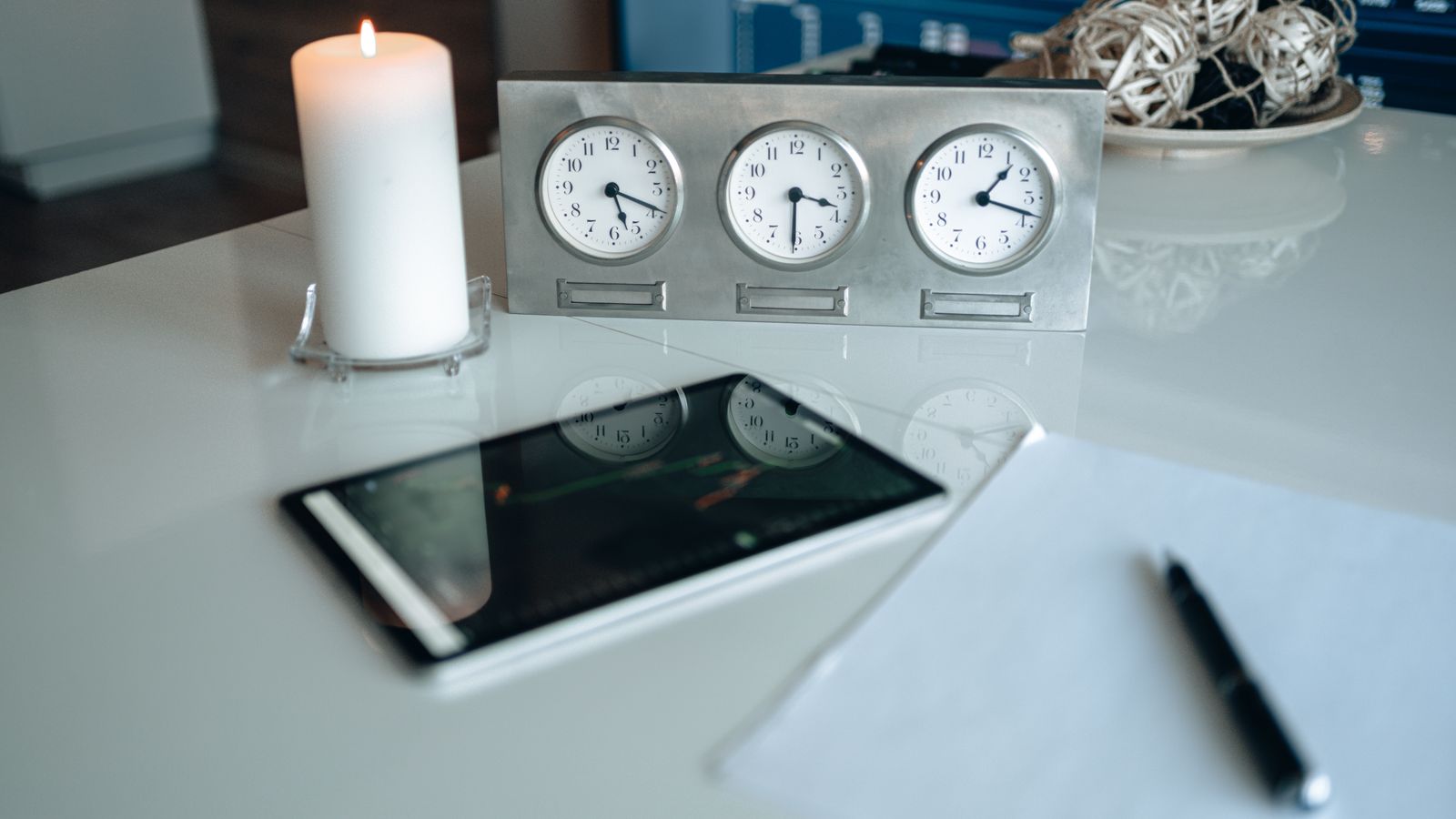 Three-dial world time clock on a desk beside a tablet and notepad