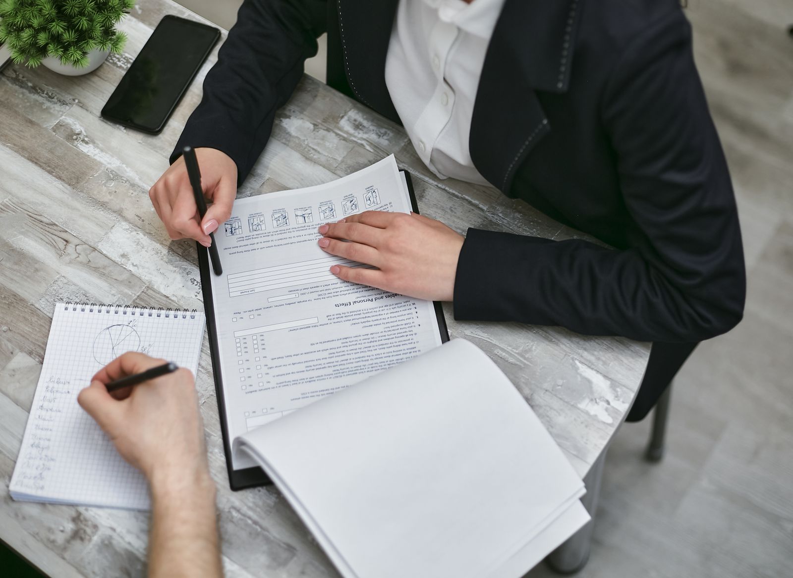 Two colleagues at a desk reviewing a printed client document and taking notes
