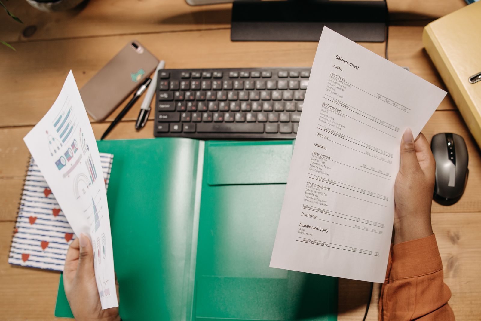 Overhead view of hands comparing a printed balance sheet against a summary chart on a desk