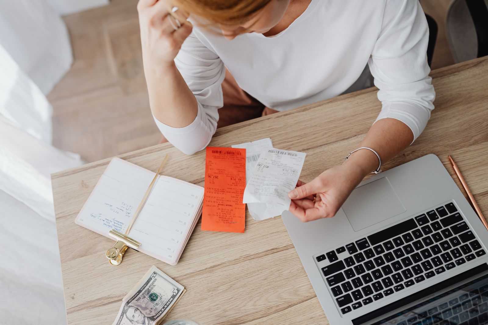 Business owner sorting paper receipts by hand at a desk beside a laptop and notebook while catching up the books