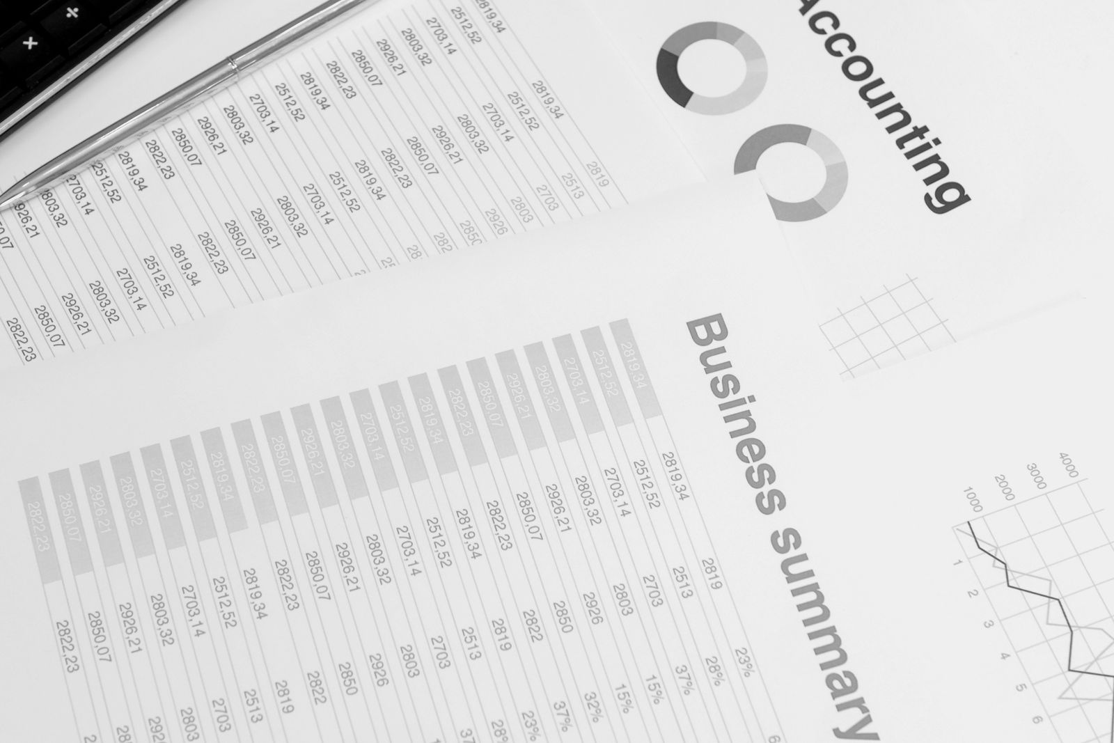 Printed accounting reports and a business summary showing numeric columns, pie charts, and a trend line spread across a desk beside a keyboard and pen