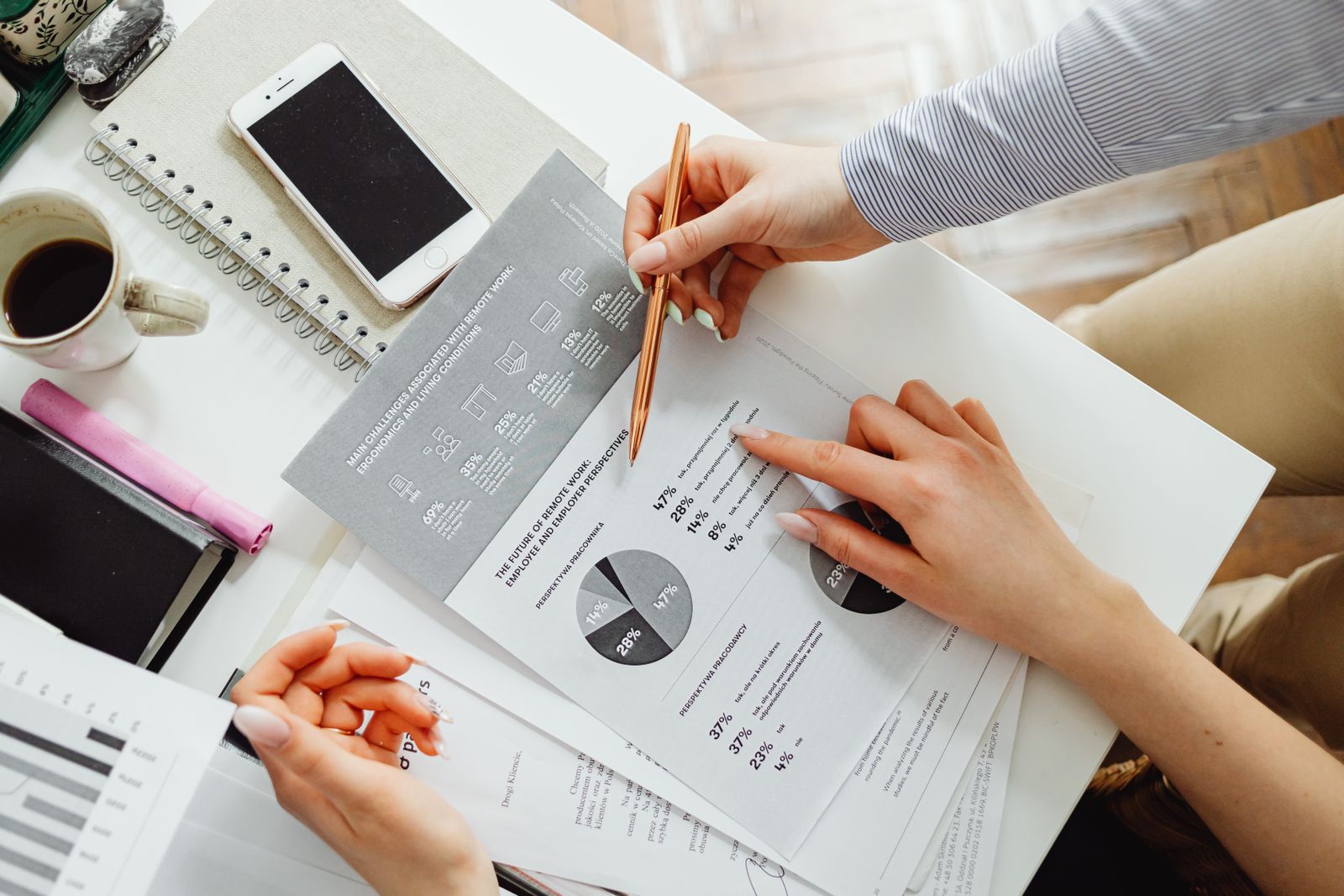 Two colleagues reviewing printed financial reports with pie charts and percentage breakdowns across a white desk