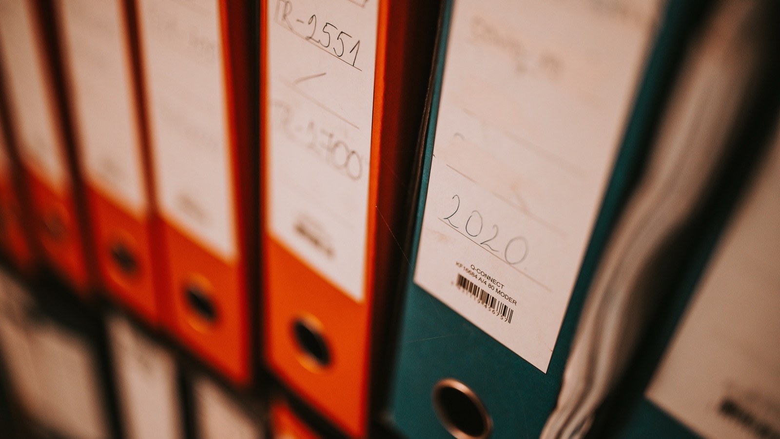 Row of orange and teal office binders on a shelf, one spine labelled with the year 2020