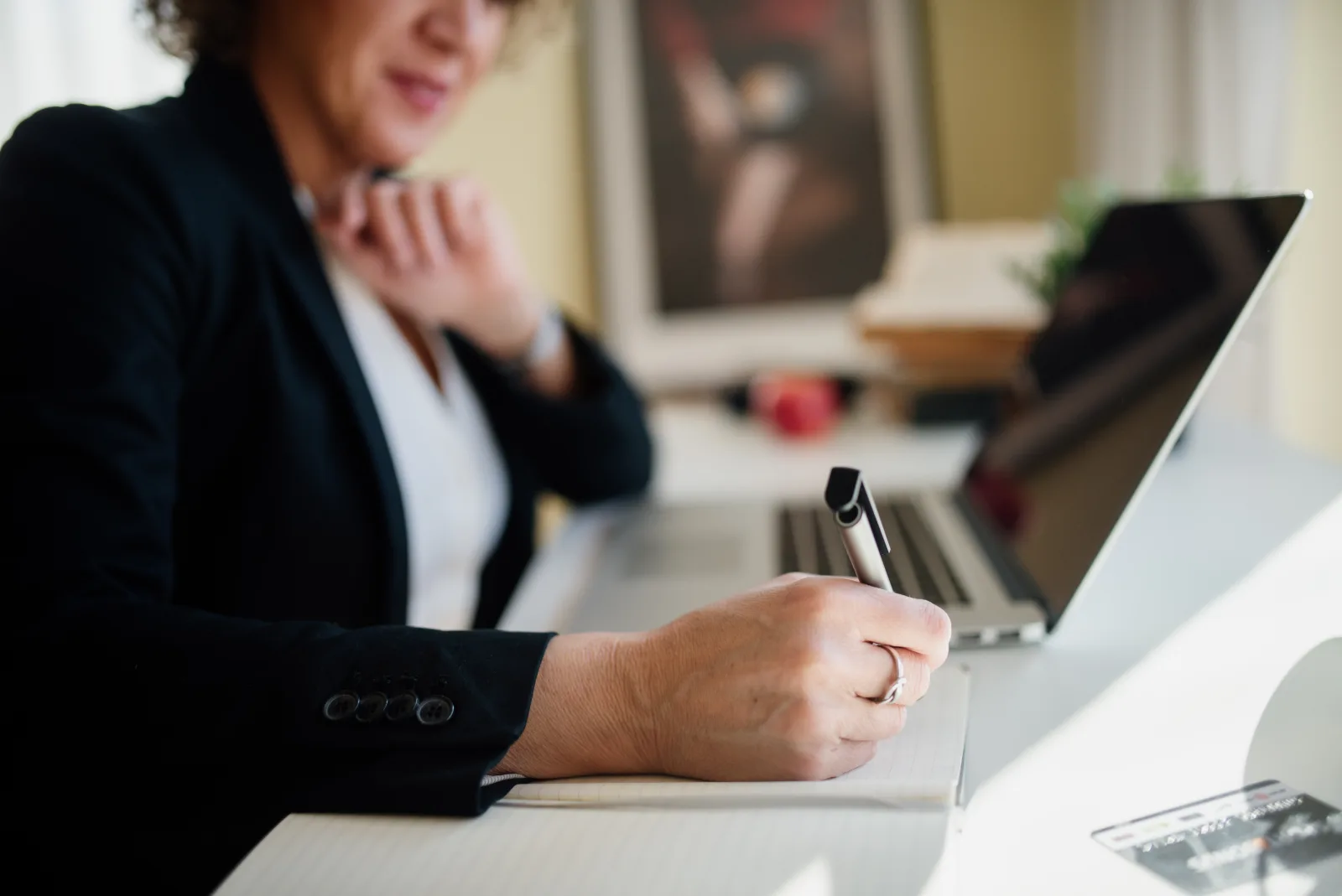 Finance professional taking handwritten notes beside a laptop during a month-end review