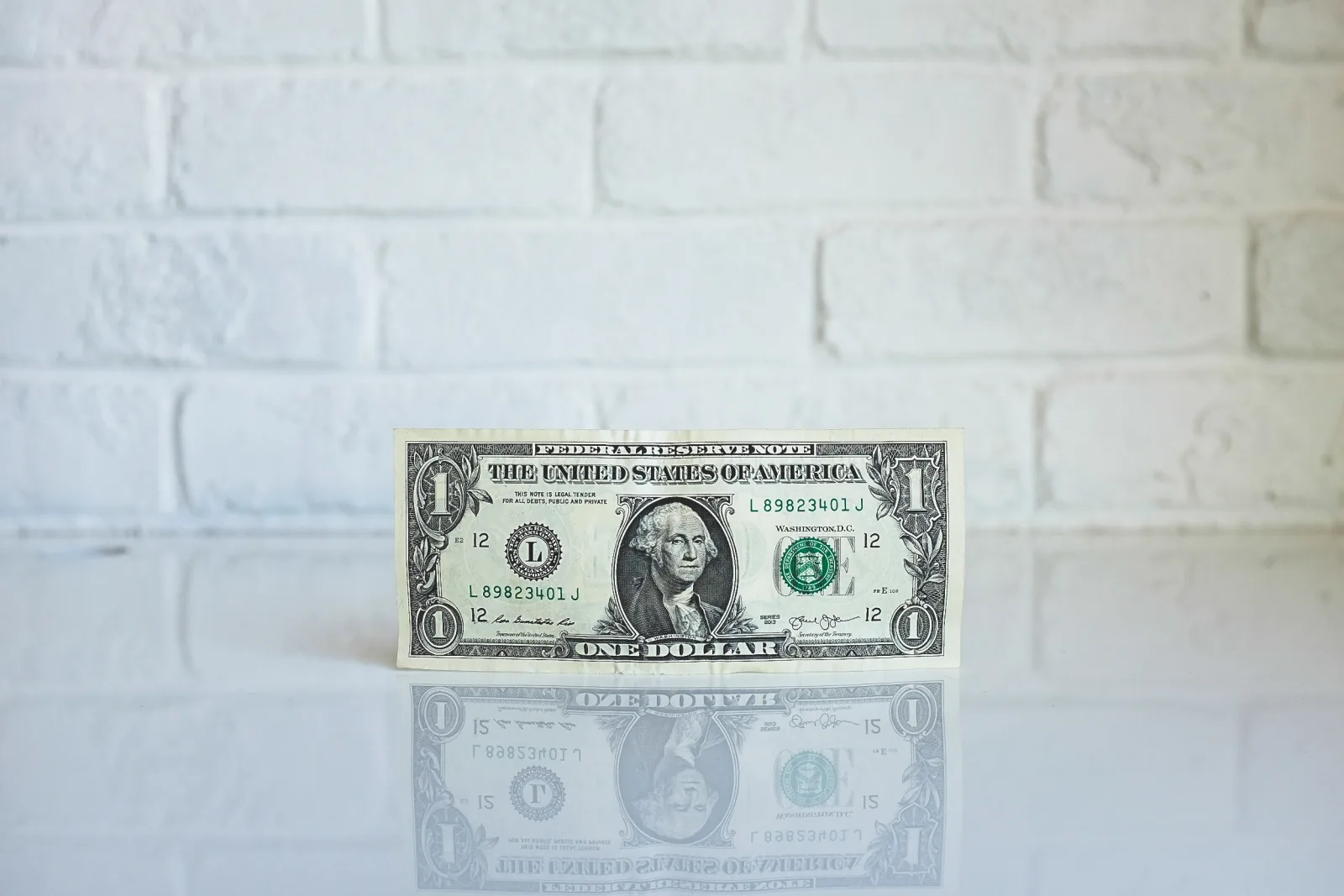 A single US one-dollar bill standing on a reflective white surface, its mirror image below it, illustrating revenue and cash as two views of the same money
