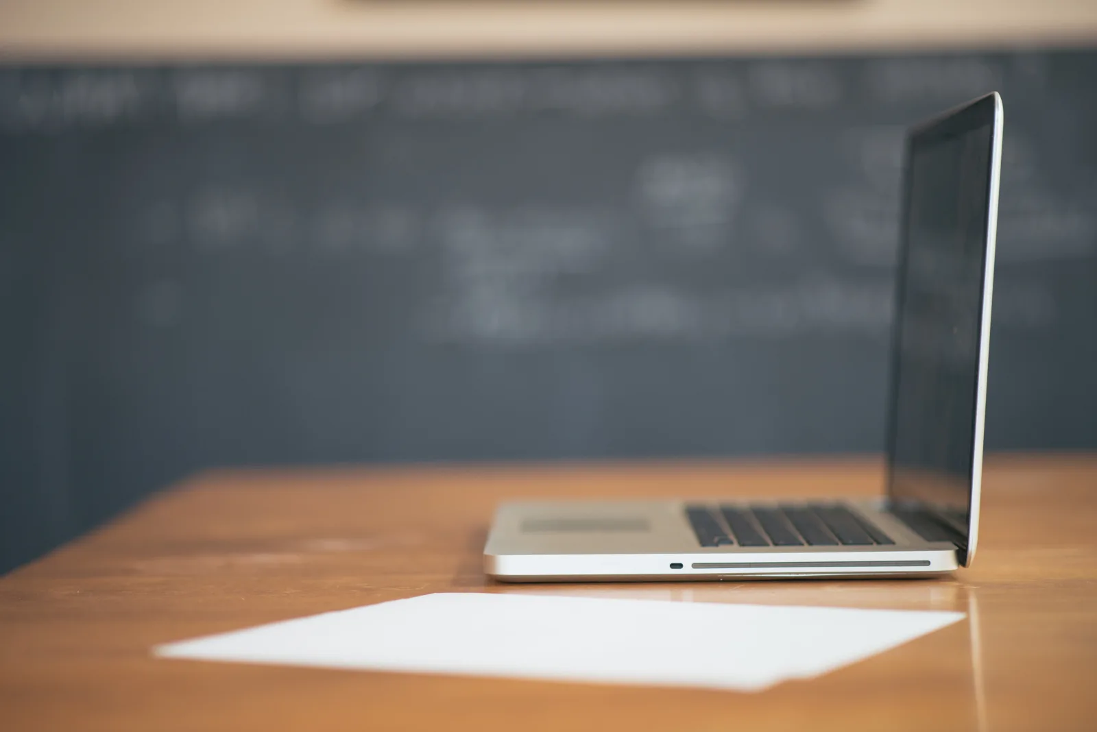 Open laptop and a blank sheet of paper on a wooden desk, representing the first weeks of an engagement with an outsourced accounting firm
